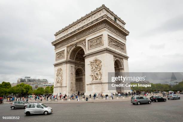 tourist visiting arc de triomphe against cloudy sky in city - arc de triomphe stock pictures, royalty-free photos & images