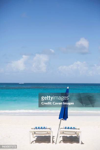 deck chairs and parasol at beach against sky during sunny day - saint martin caraibi stock-fotos und bilder