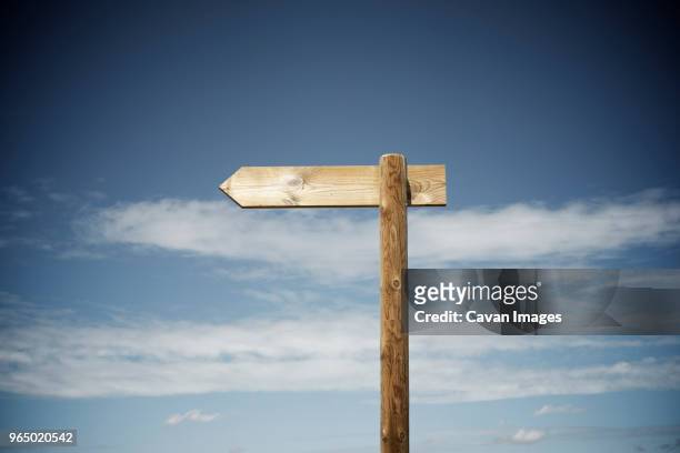 wooden arrow sign against cloudy sky - wooden sign stock-fotos und bilder