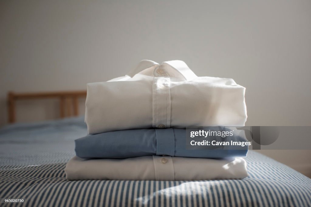 Close-up of folded shirts stacked on bed at home