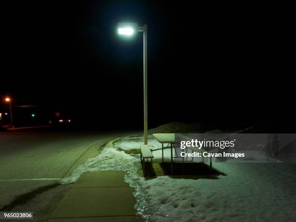 table and benches on snow at sidewalk by illuminated street light during night in city - snow melting on sidewalk stock pictures, royalty-free photos & images