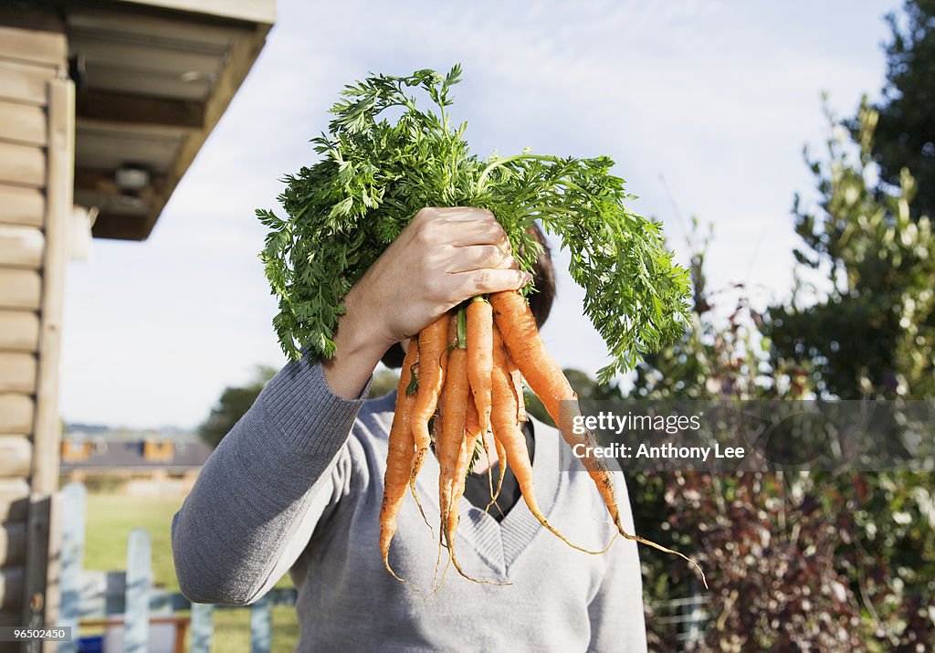 Woman hiding face behind carrots