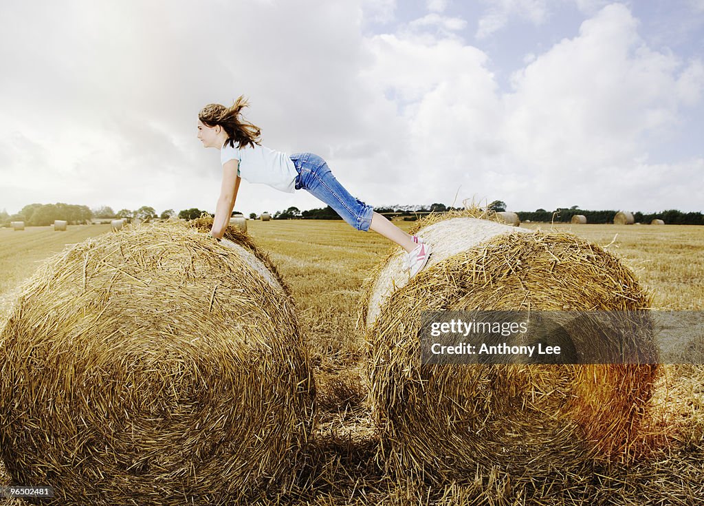 Girl balancing between two bales of hay