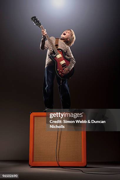 boy playing electric guitar standing on speaker - solo bambini maschi foto e immagini stock