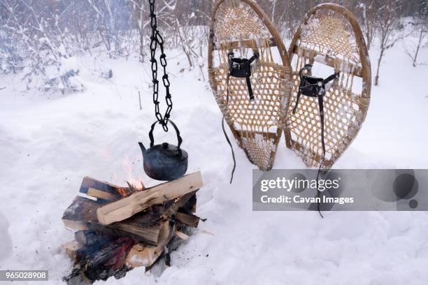 kittle hanging over campfire by snowshoes on snow covered field - kittle stock pictures, royalty-free photos & images