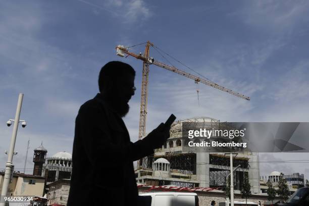 Pedestrian looks at a mobile phone as he walks past an under-construction mosque in Taksim square in Istanbul, Turkey, on Tuesday, May 29, 2018....