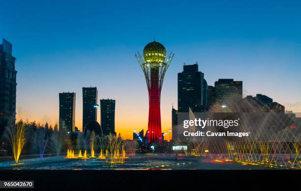 illuminated bayterek tower and fountain in city against clear blue sky - astana stockfoto's en -beelden