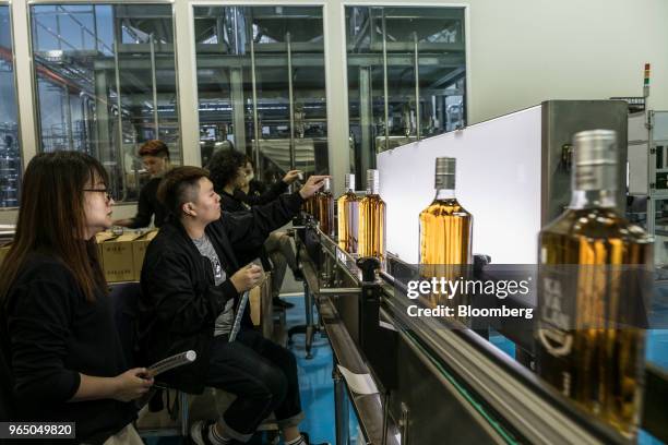 Employees apply caps to bottles of Kavalan whisky moving along a conveyor at the Kavalan Single Malt Whisky distillery stands in Yilan County,...