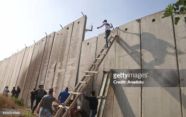 Palestinians climb the ladders to cross the separation wall to reach Jerusalem in order to perform the third Friday Prayer of Islamic holy month of...