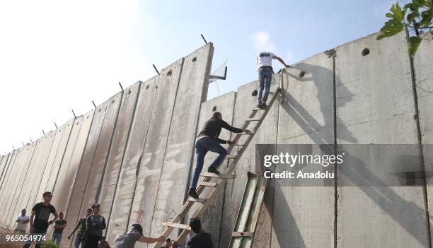 Palestinians climb the ladders to cross the separation wall to reach Jerusalem in order to perform the third Friday Prayer of Islamic holy month of...