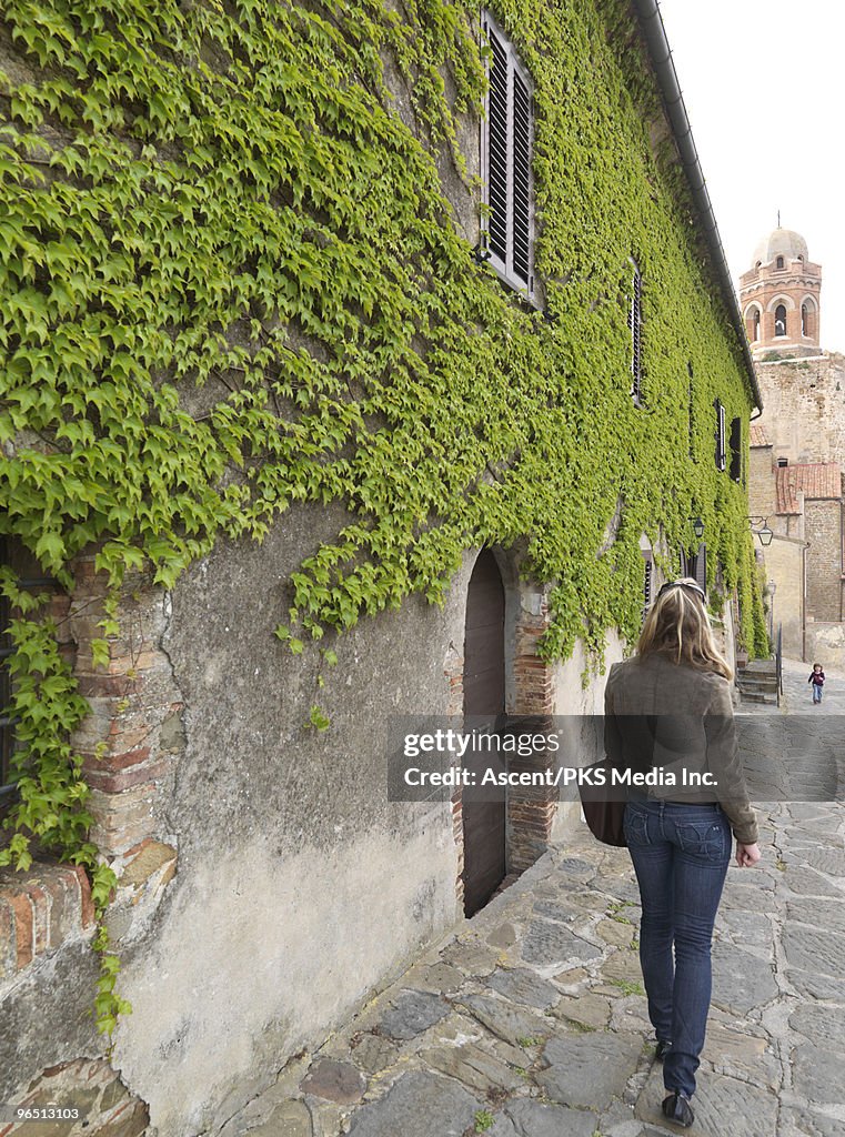 Woman walks towards child on leafy medieval street