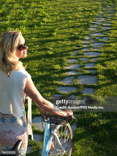 woman pushes bike along stone pathway - vista trasera de tres cuartos fotografías e imágenes de stock