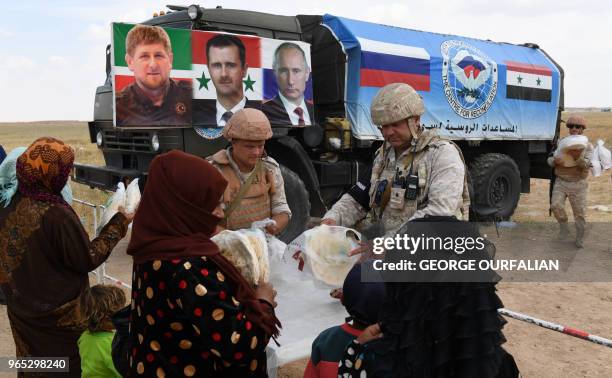 Members of the Russian military police hand out food aid provided by a Chechen charity to Syrians queueing up after arriving in a convoy returning...