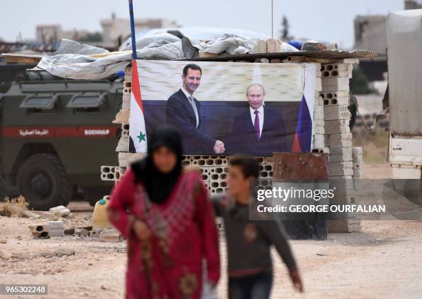 Syrian woman walks with a boy past a banner showing Russian President Vladimir Putin shaking hands with Syrian President Bashar al-Assad, after...