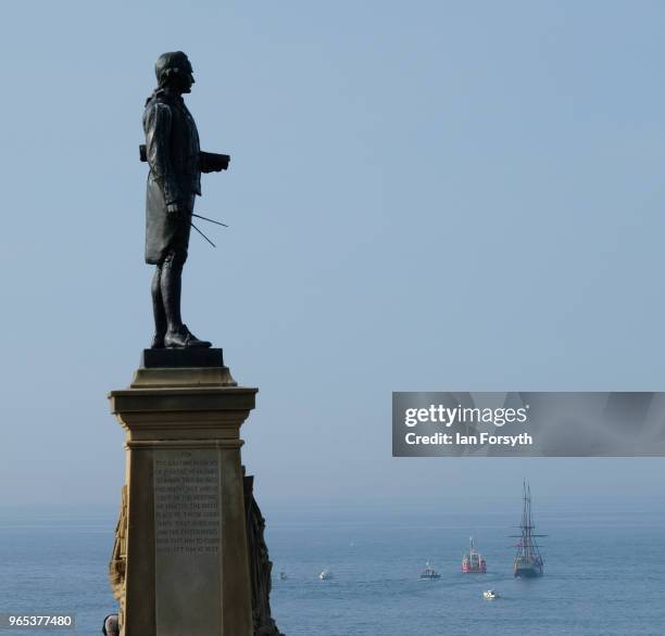 The statue of Captain James Cook stand proud as a full sized replica of Captain Cook's famous ship, the HM Bark Endeavour is towed into Whitby...