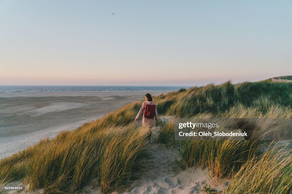 Kvinnan promenader nära havet på ön Texel i solnedgången