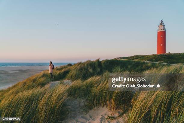 frau in der nähe von leuchtturm auf der insel texel bei sonnenuntergang - niederlande stock-fotos und bilder