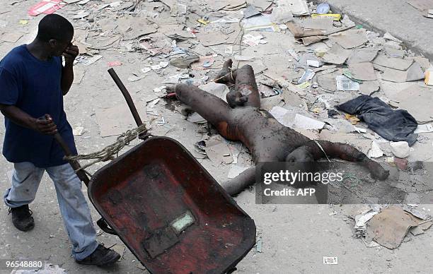 Haitian man pushing a wheelbarrow passes by a rotting corpse lying on the street amid the rubble in Port-au-Prince, January 19, 2010. The tens of...