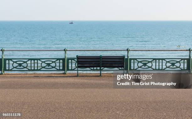 view of a boat, the sea and an empty bench and railings, along the promenade, brighton, uk - promenade stock pictures, royalty-free photos & images