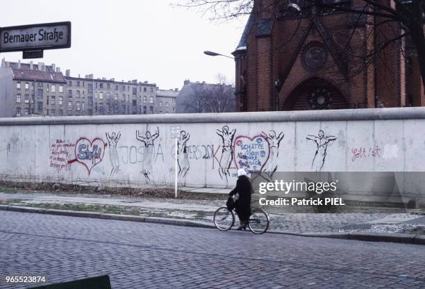 Femme à vélo passant devant le mur de Berlin, en Allemagne de l'Ouest le 15 mai 1984.