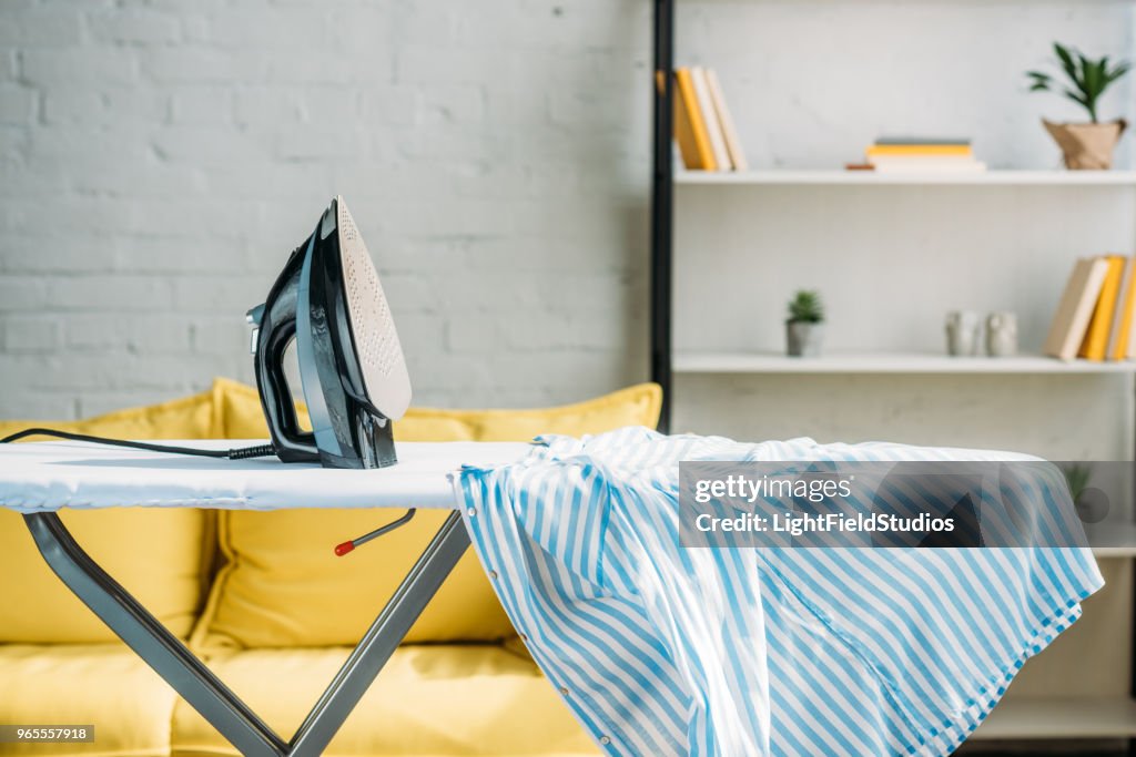 Striped blue shirt and iron on ironing board at home