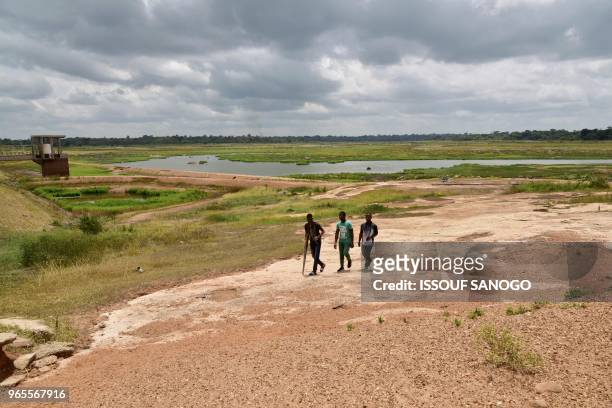 Three men walk near the Asseche Dam of the Company of Distribution of water of Ivory Coast in Angoua-Yaokro near Bouaké, on June 1, 2018. - The...