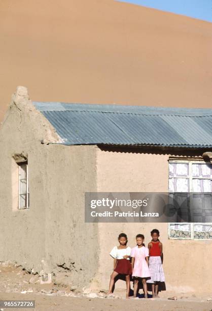 Portrait of three girls as they stand against the wall of a house in the Kalahari Desert, South Africa, 1985.