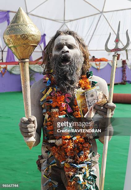 An Indian Sadhu holds a mace and a fistful of US dollars and Indian Rupees as he poses at Pilot Baba's Camp in Haridwar on February 11 on the eve of...