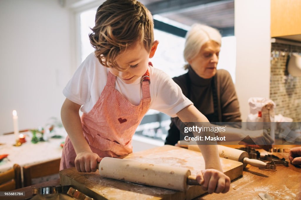 Boy rolling dough while standing by grandmother at kitchen counter