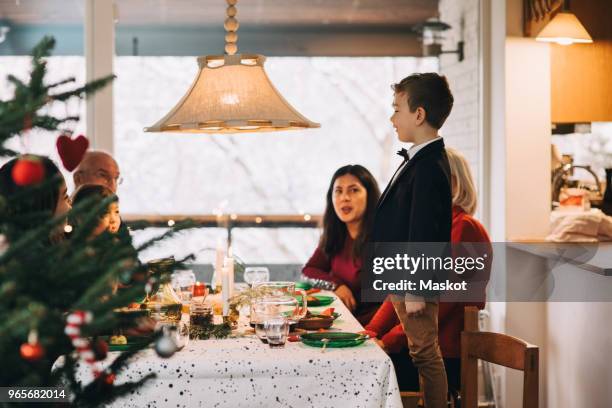 boy talking to family while standing on chair during christmas meal at table - national day in sweden 2017 stock pictures, royalty-free photos & images