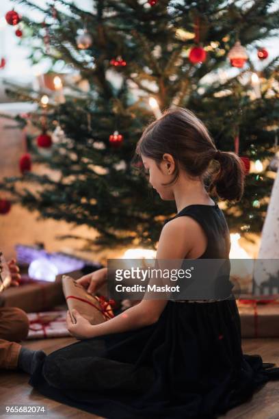 girl looking at presents while sitting by christmas tree in home - national day in sweden 2017 stockfoto's en -beelden