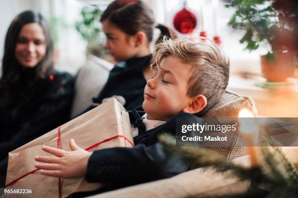 smiling boy holding christmas present while sitting with family in living room - julklappar bildbanksfoton och bilder