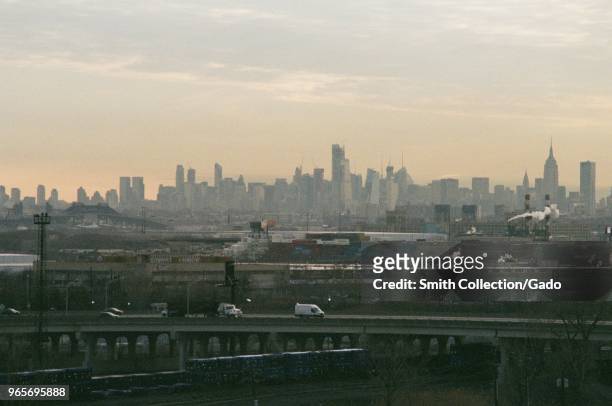 Cars drive through an industrial portion of Newark, New Jersey on a hazy morning at rush hour, with the skyline of Manhattan, New York City in the...