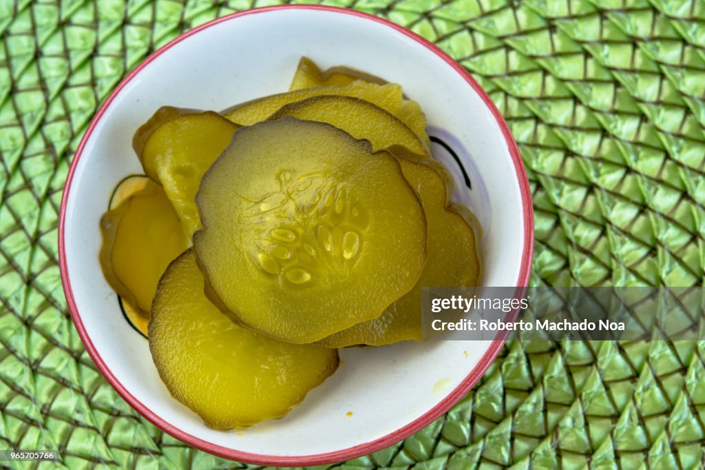 Cucumber pickles served on a white small bowl and over a green textured background
