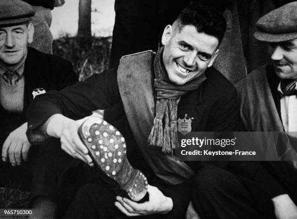 Un marcheur montre au photographe la semelle renforcée d'une de ses bottes pour qu'elle tienne toute la marche, au Royaume-Uni le 29 octobre 1936.