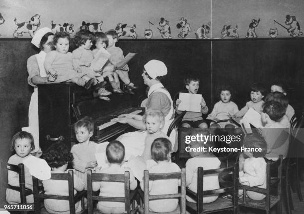 De jeunes enfants répètent des chants de Noël avec l'accompagnement au piano de leur gouvernante dans une crèche, le 14 décembre 1933 au Royaume-Uni.