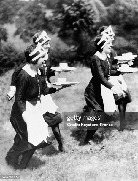 Gouvernantes vêtues de leur tablier blanc, col et bonnet blanc, portant plateau et bol, photographiées pendant leur course aux environs de Londres,...