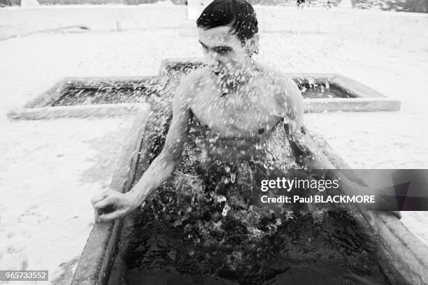 Un jeune homme russe plonge dans l'eau glacée dans le cadre du rituel orthodoxe russe de l'Epiphanie. Chaque année, un crucifix est sculpté dans le...