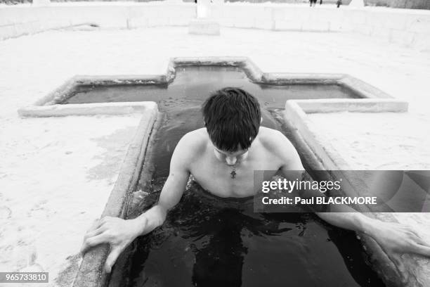 Un jeune homme russe plonge dans l'eau glacée dans le cadre du rituel orthodoxe russe de l'Epiphanie. Chaque année, un crucifix est sculpté dans le...