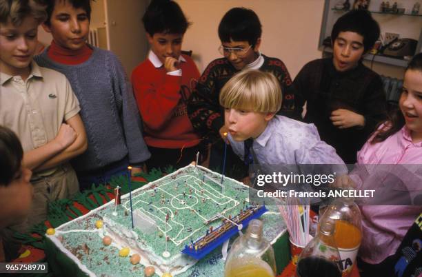Enfant soufflant les bougies de son gâteau d'anniversaire en forme de terrain de football, le 24 mars 1989, France.