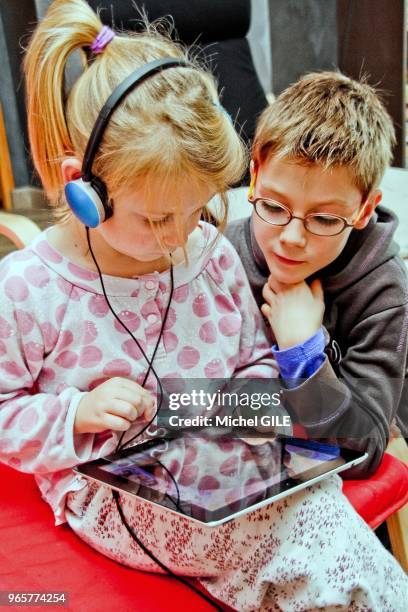 Petit garcon de 9 ans regardant sa petite soeur de six ans jouer avec sa tablette numérique en ecoutant de la musique.