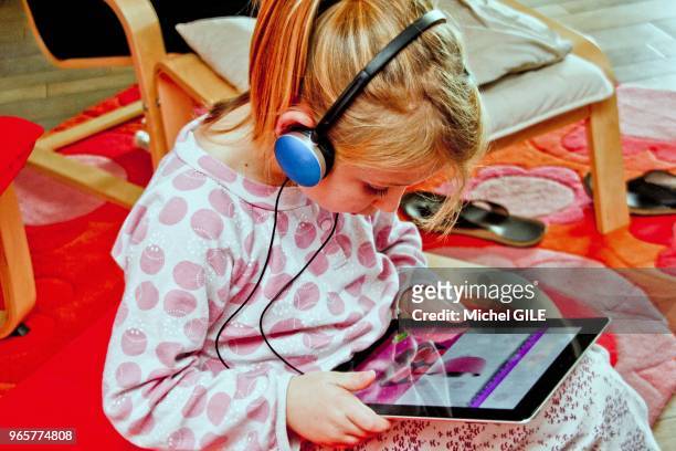 Petite fille de six ans ecoutant de la musique avec un casque et une tablette numérique.