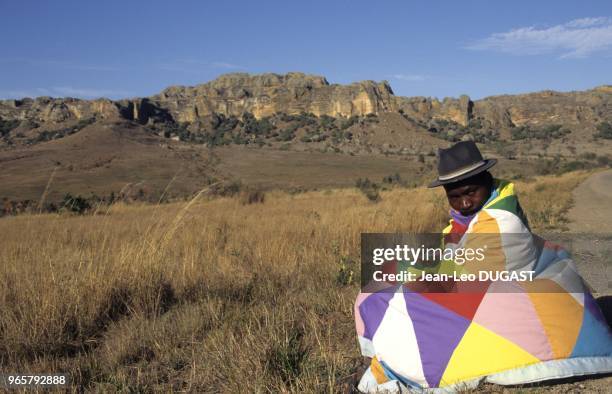 Hautes-Terres. Au bord de la route, un homme enveloppé d'une couverture attend l'autobus. Hautes-Terres. Au bord de la route, un homme enveloppé...