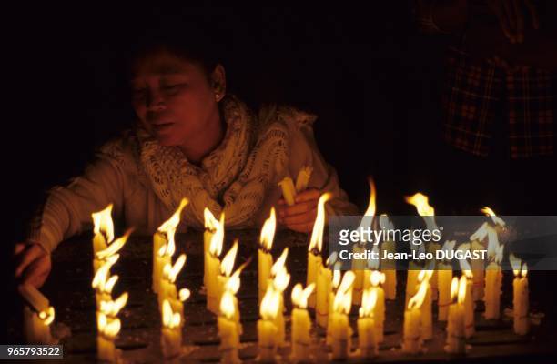 Femme allumant des bougies près d'une statue de Bouddha, avant de se mettre en prières. Femme allumant des bougies près d'une statue de Bouddha,...