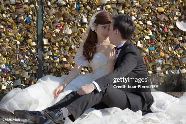 Les cadenas, que les amoureux et touristes venant du monde entier accrochent au Pont des Arts vont. Des jeunes mariés asiatique posent devant des...