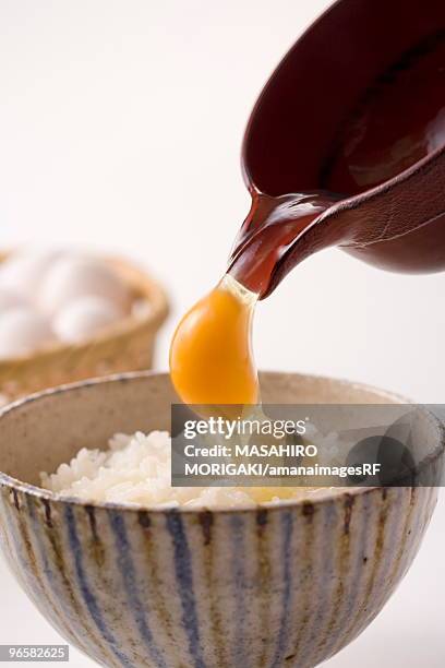 row egg being poured on bowl of rice, white background - egg white background stock-fotos und bilder