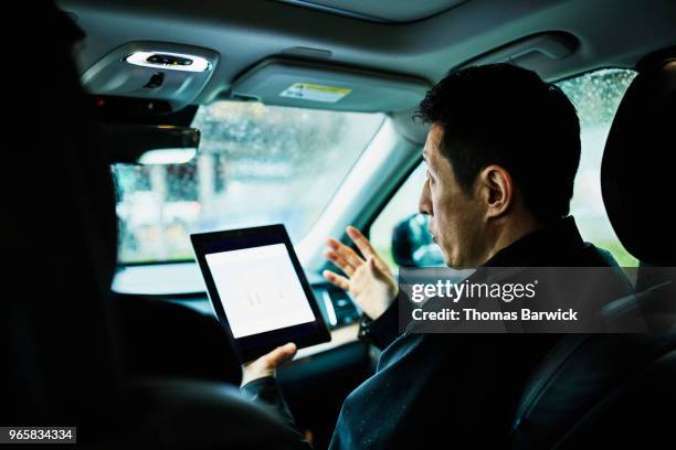 businessman explaining data on digital tablet to colleague while sitting in car before client meeting - gedeelde mobiliteit stockfoto's en -beelden