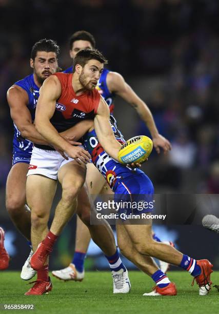 Jack Viney of the Demons handballs whilst being tackled by Tom Boyd and Caleb Daniel of the Bulldogs during the round 11 AFL match between the...