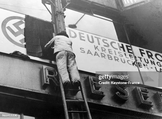 Un ouvrier pose un rideau noir devant la croix gammée figurant sur l'enseigne du 'Front allemand' car toute exhibition de drapeaux ou d'emblème...