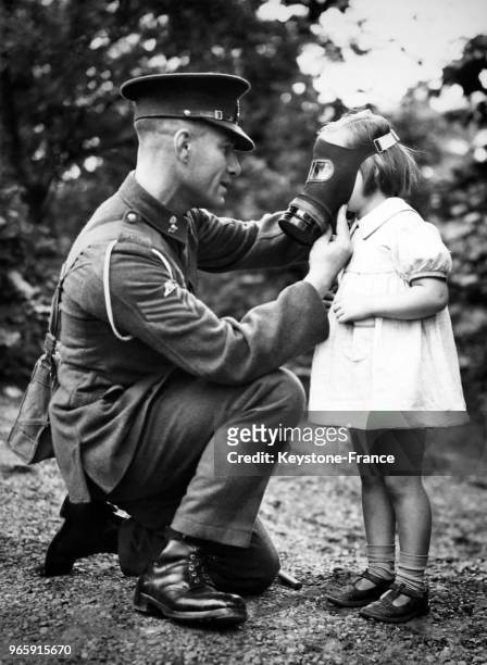 Un soldat ajuste un masque à gaz sur le visage d'une petite fille à la caserne de Woolwich, Londres, Royaume-Uni le 27 juillet 1939.